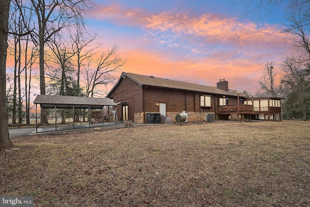 back of house featuring a deck, cooling unit, stone siding, a yard, and a chimney