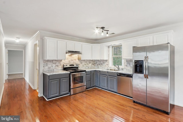 kitchen featuring appliances with stainless steel finishes, gray cabinets, under cabinet range hood, white cabinetry, and a sink