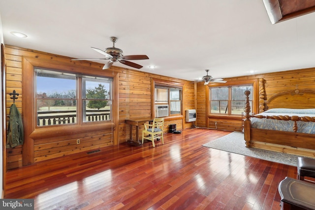 bedroom with cooling unit, wooden walls, visible vents, heating unit, and hardwood / wood-style floors