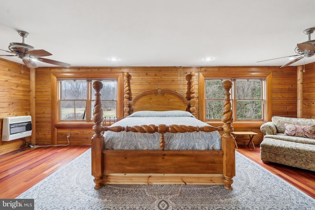 bedroom with heating unit, multiple windows, log walls, and wood finished floors