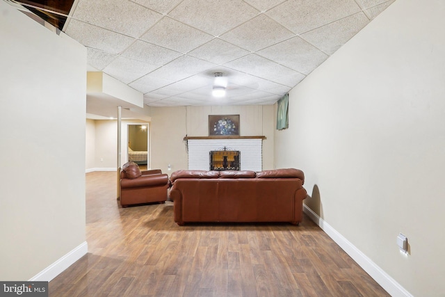 living area with a paneled ceiling, a brick fireplace, baseboards, and wood finished floors