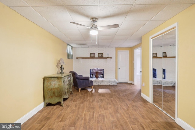 living area featuring a paneled ceiling, ceiling fan, baseboards, and wood finished floors