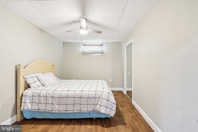 bedroom with a ceiling fan, wood finished floors, a paneled ceiling, and baseboards