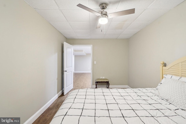 unfurnished bedroom featuring a ceiling fan, a paneled ceiling, baseboards, and wood finished floors