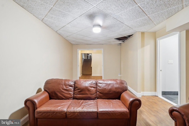 living room with light wood-type flooring, visible vents, baseboards, and a drop ceiling