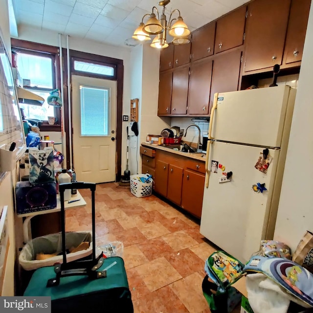 kitchen featuring freestanding refrigerator, hanging light fixtures, light countertops, a chandelier, and a sink