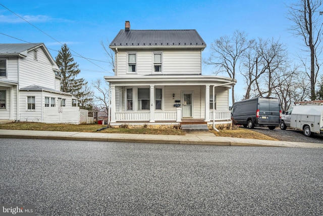 view of front of house featuring covered porch, a chimney, and metal roof