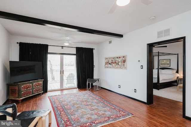 interior space featuring visible vents, a ceiling fan, a textured ceiling, wood finished floors, and beamed ceiling