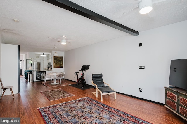 sitting room featuring a textured ceiling, beam ceiling, wood finished floors, and a ceiling fan