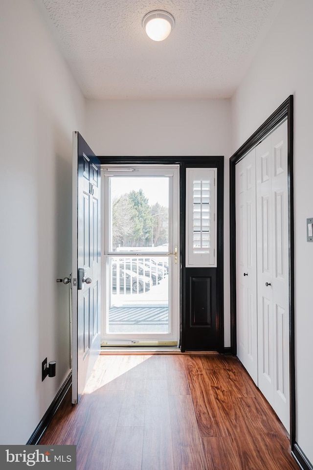 doorway to outside featuring a textured ceiling, baseboards, and wood finished floors