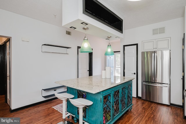 kitchen with dark wood finished floors, visible vents, freestanding refrigerator, a textured ceiling, and light stone countertops