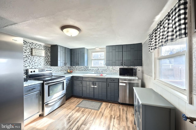 kitchen featuring stainless steel appliances, gray cabinets, light countertops, light wood-style flooring, and a sink