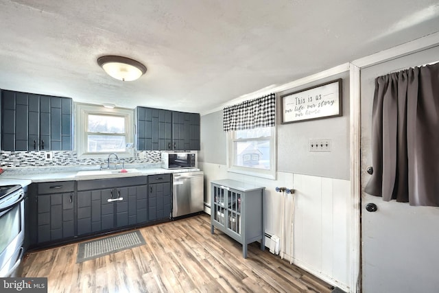 kitchen featuring a wainscoted wall, gray cabinets, stainless steel appliances, a baseboard heating unit, and a sink