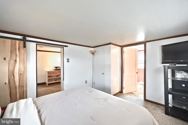 bedroom with carpet, crown molding, a barn door, ensuite bath, and baseboards