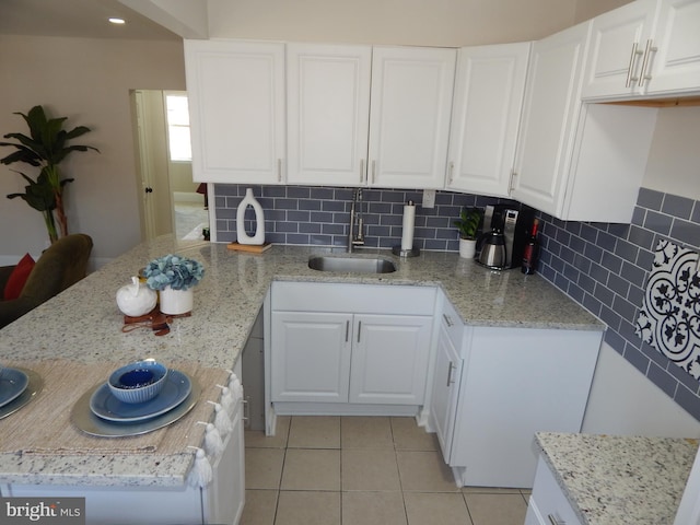 kitchen with light stone counters, decorative backsplash, white cabinetry, a sink, and a peninsula