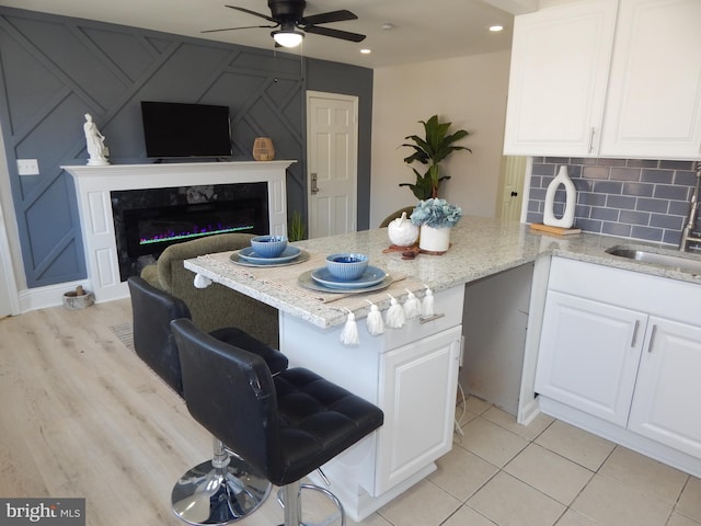 kitchen featuring light stone counters, a peninsula, a sink, white cabinets, and backsplash