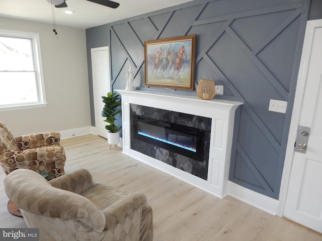 living area featuring ceiling fan, wood finished floors, a glass covered fireplace, and baseboards