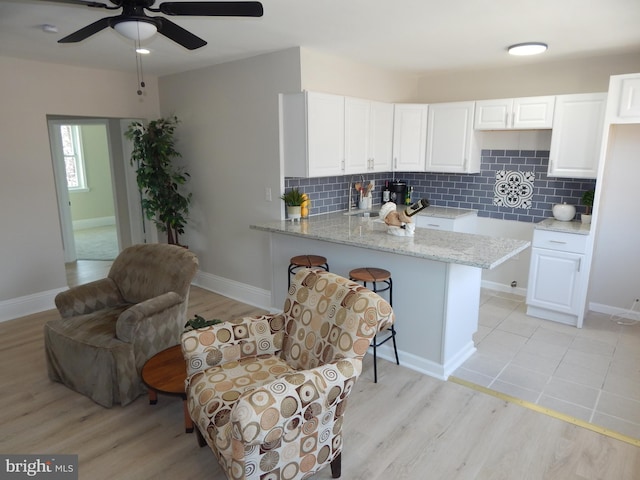 kitchen with light wood-type flooring, white cabinets, a peninsula, and light stone countertops