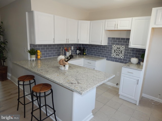 kitchen featuring a peninsula, a breakfast bar, white cabinetry, decorative backsplash, and light stone countertops