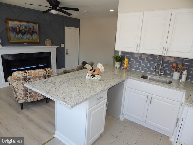 kitchen with a fireplace, decorative backsplash, white cabinets, a sink, and a peninsula