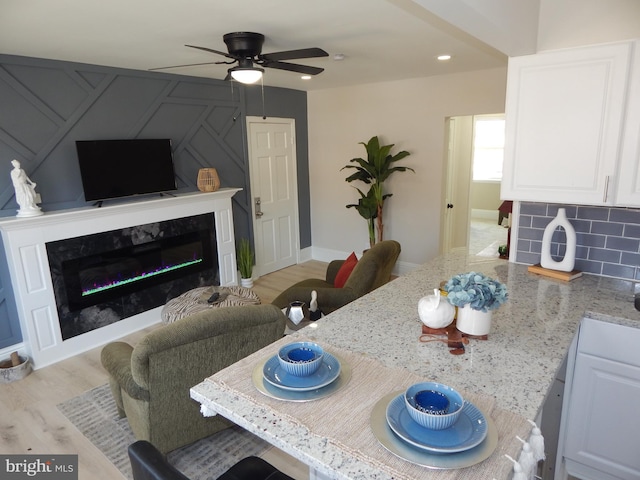 dining room featuring light wood finished floors, recessed lighting, a high end fireplace, ceiling fan, and baseboards