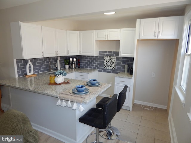 kitchen with a peninsula, a kitchen bar, white cabinetry, and decorative backsplash