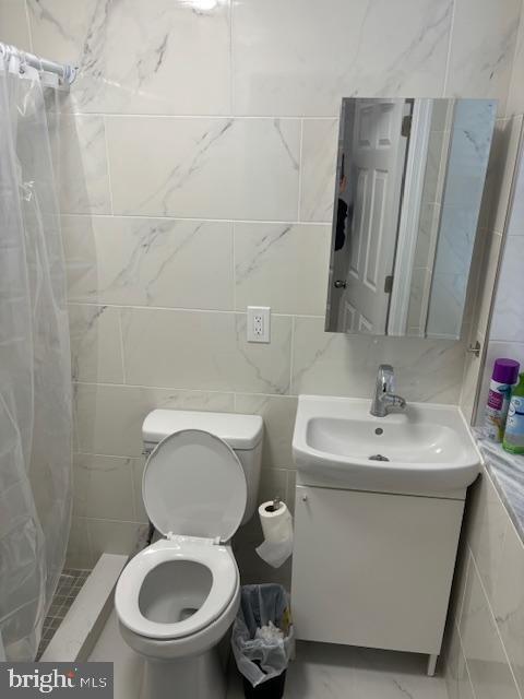 full bathroom featuring toilet, a shower with shower curtain, vanity, tile walls, and marble finish floor