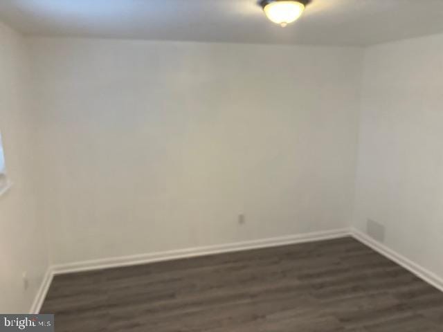 unfurnished room with baseboards and dark wood-type flooring