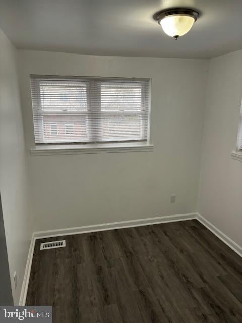 unfurnished room featuring dark wood-style floors, visible vents, and baseboards