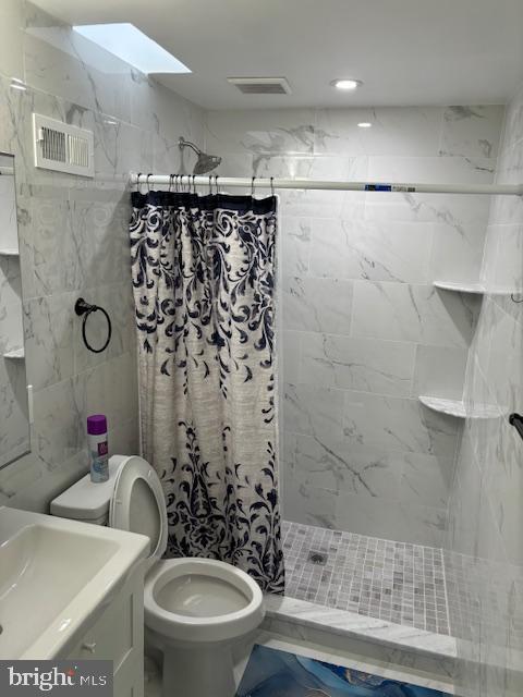 full bathroom featuring a stall shower, a skylight, visible vents, and toilet