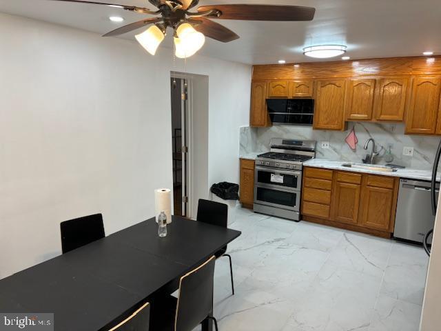 kitchen featuring marble finish floor, appliances with stainless steel finishes, brown cabinetry, and decorative backsplash