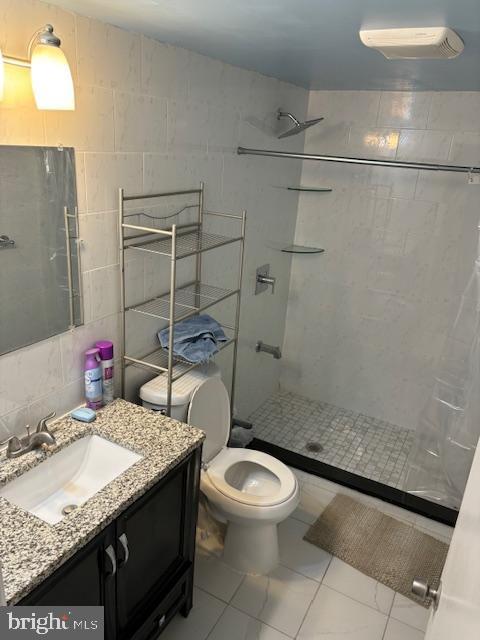 full bathroom with a tile shower, tile walls, toilet, and vanity