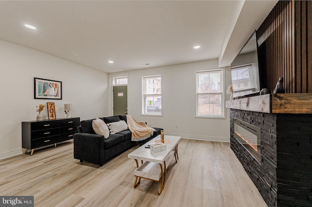 living area featuring light wood-style floors, recessed lighting, baseboards, and a glass covered fireplace