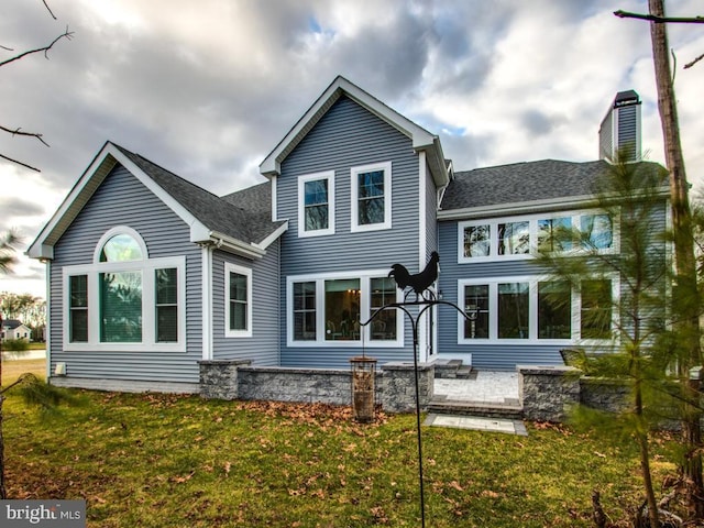 back of property featuring a patio area, roof with shingles, a yard, and a chimney