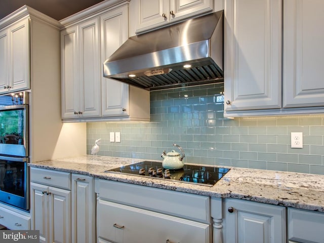 kitchen featuring light stone countertops, black electric stovetop, under cabinet range hood, double oven, and backsplash