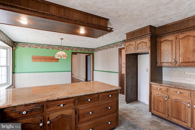 kitchen featuring a textured ceiling, wainscoting, decorative light fixtures, and brown cabinets