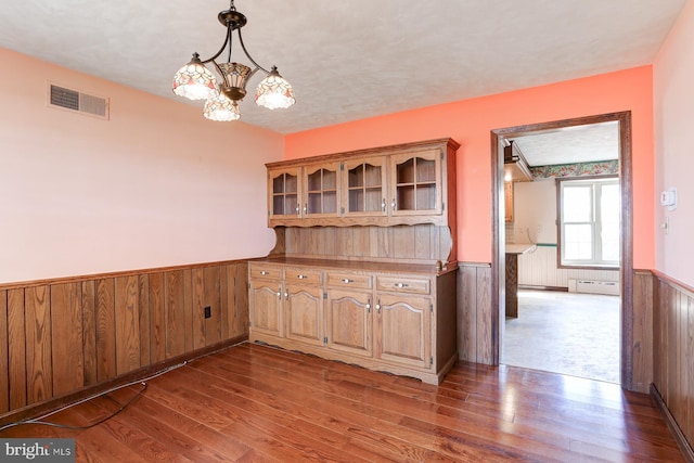 unfurnished dining area with wooden walls, visible vents, dark wood finished floors, a wainscoted wall, and an inviting chandelier