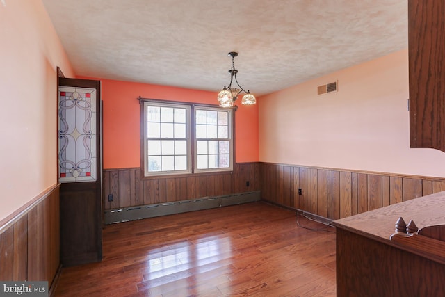 unfurnished dining area featuring a baseboard radiator, visible vents, wainscoting, a textured ceiling, and hardwood / wood-style flooring