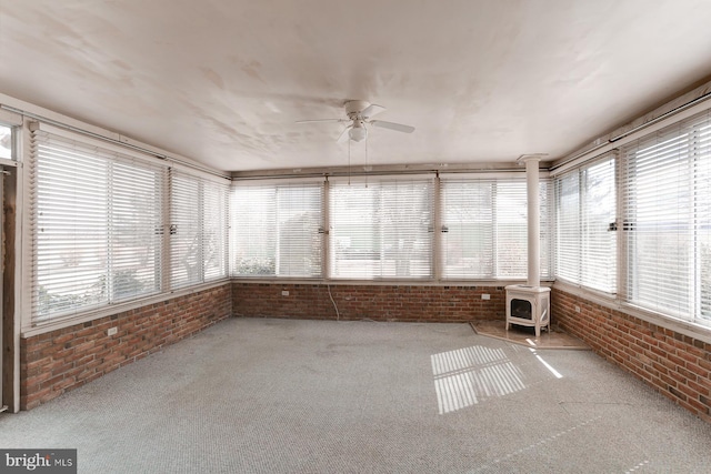 unfurnished sunroom featuring a ceiling fan and a wood stove