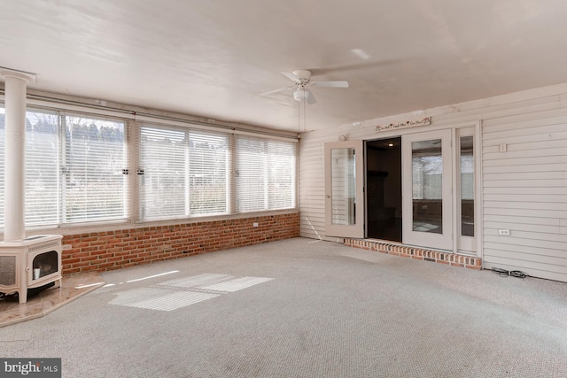 unfurnished sunroom featuring a wood stove, heating unit, and ceiling fan