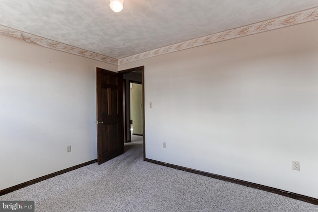 spare room featuring light carpet, a textured ceiling, and baseboards