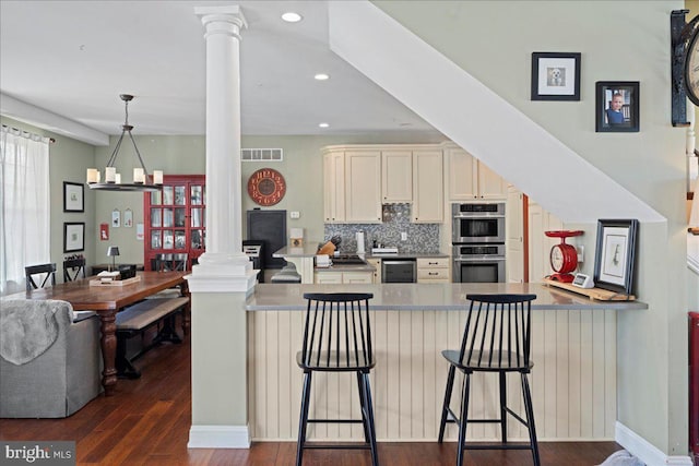 kitchen featuring dark wood-style floors, decorative columns, tasteful backsplash, visible vents, and double oven