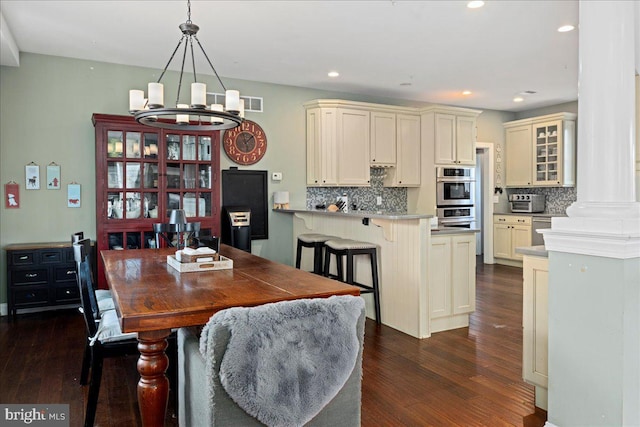 dining area with ornate columns, a chandelier, dark wood finished floors, and recessed lighting