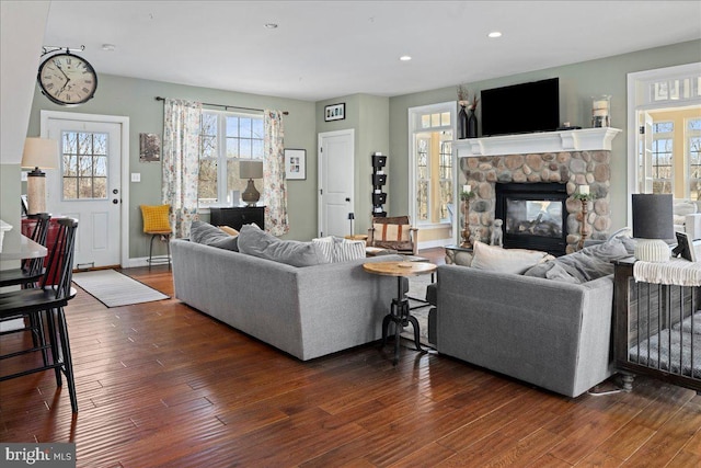 living area featuring recessed lighting, baseboards, dark wood-style flooring, and a stone fireplace