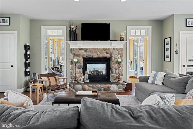 living room featuring a stone fireplace, wood finished floors, and baseboards