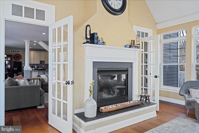 living room with a glass covered fireplace, lofted ceiling, ornate columns, and wood finished floors