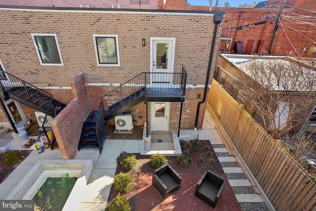 rear view of property with ac unit, brick siding, a patio area, a fenced backyard, and stairs