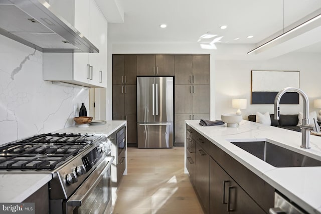 kitchen with appliances with stainless steel finishes, a sink, dark brown cabinetry, light stone countertops, and under cabinet range hood