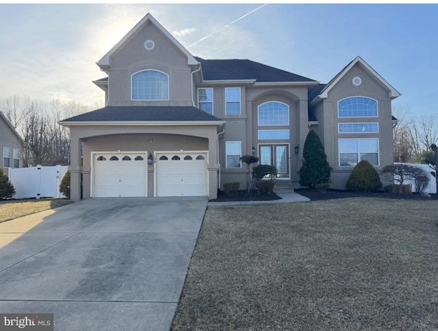 traditional-style home featuring roof with shingles, stucco siding, concrete driveway, an attached garage, and fence