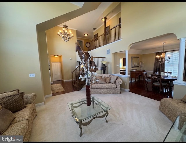 carpeted living area with arched walkways, decorative columns, a towering ceiling, a chandelier, and stairs